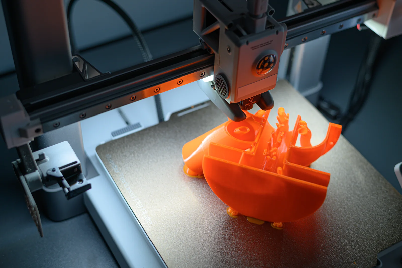 3D-принтер создаёт оранжевую деталь слой за слоем